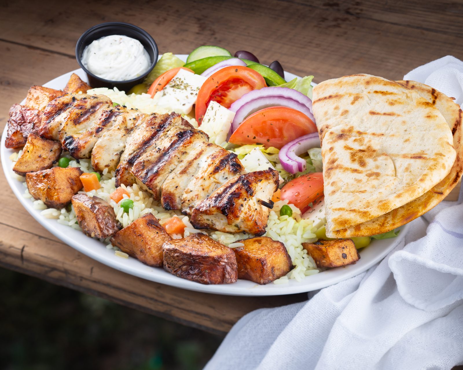 Chicken souvlaki platter with roasted potatoes, rice pilaf, Greek salad and pita